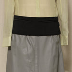 Light green shirt over gray skirt with black waistband on a beige background