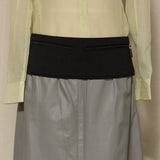 Light green shirt over gray skirt with black waistband on a beige background