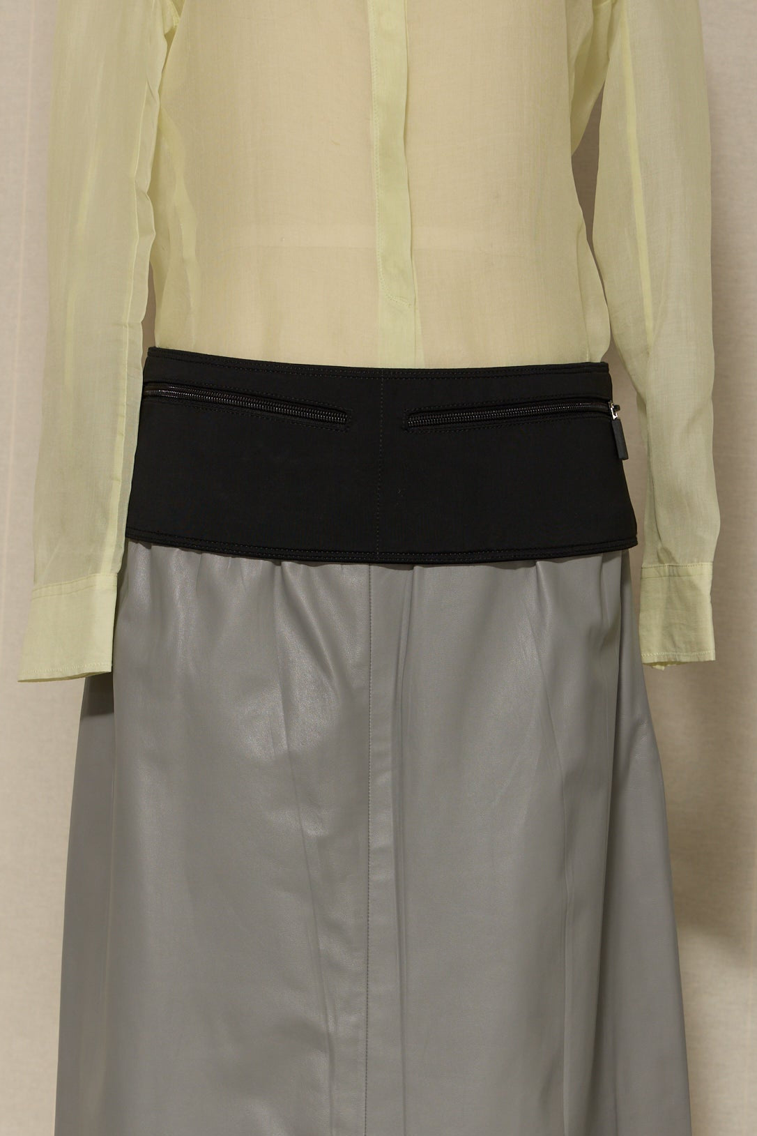 Light green shirt over gray skirt with black waistband on a beige background
