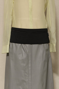 Light green shirt over gray skirt with black waistband on a beige background