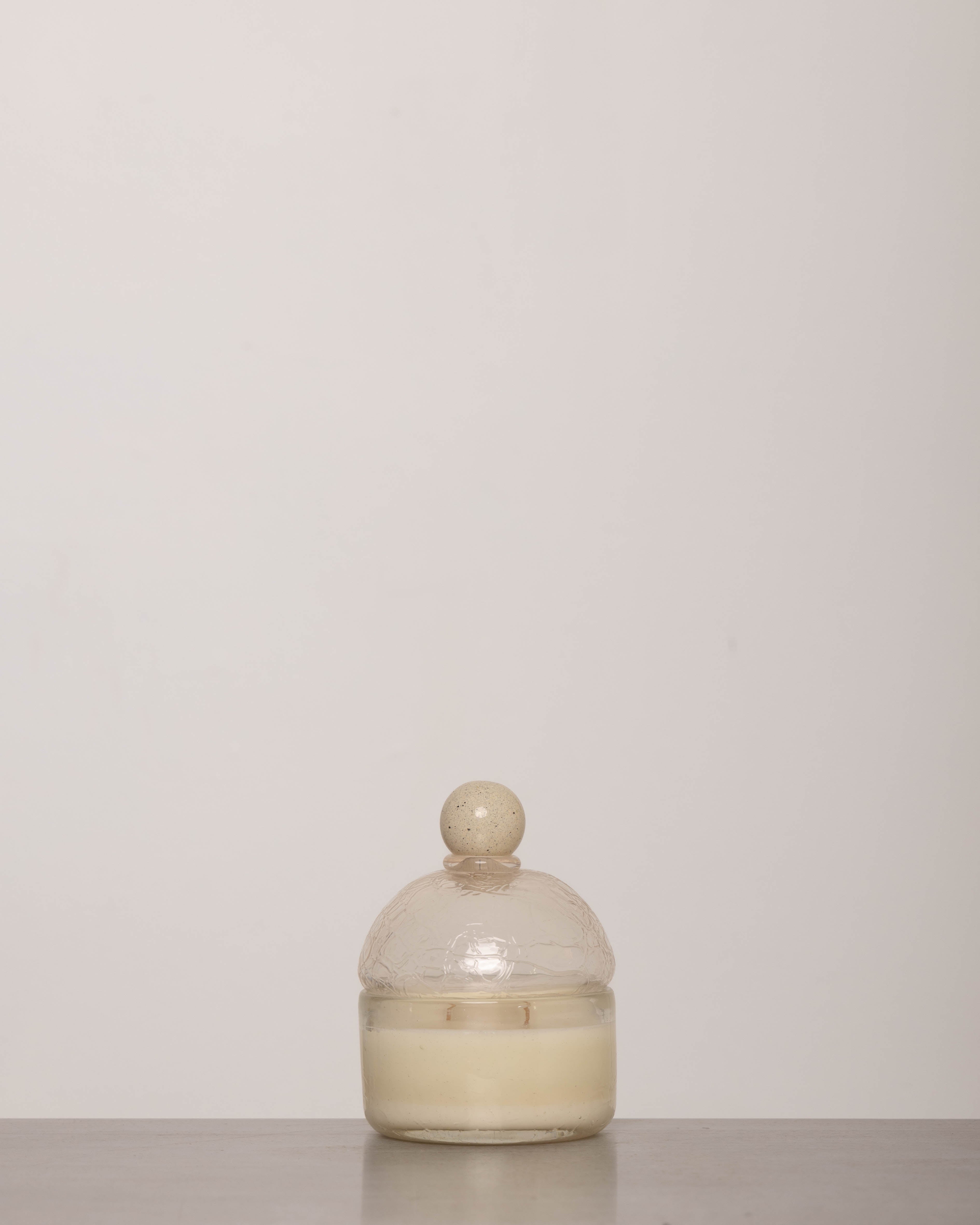 Discover the YAKUSH Candle Snow Queen – a 7" tall soy candle in hand-blown recycled glass, scented with oud, rose, and patchouli, with a 70-hour burn time.